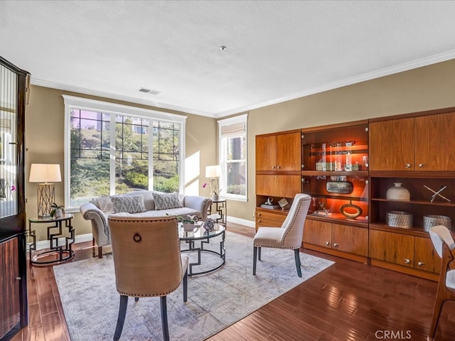 living area featuring baseboards, visible vents, wood finished floors, and ornamental molding