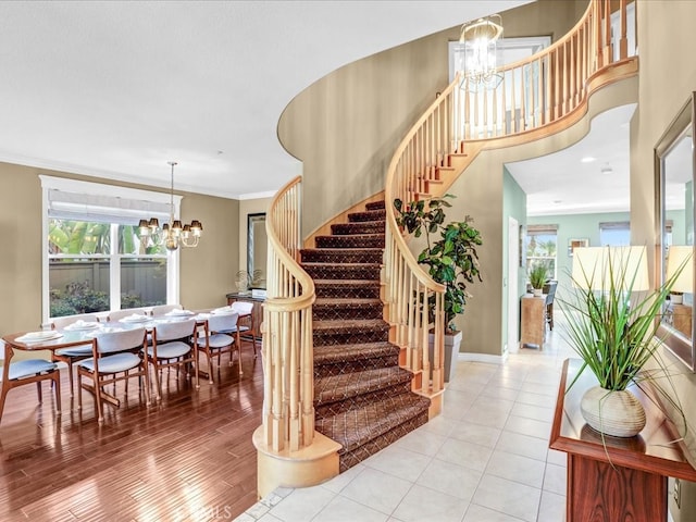 stairs with ornamental molding, wood finished floors, plenty of natural light, and an inviting chandelier