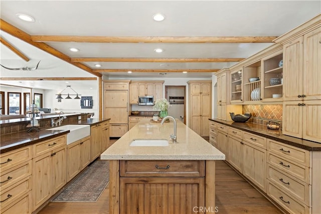 kitchen with beamed ceiling, dark wood-type flooring, sink, and a center island with sink