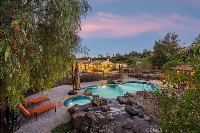 pool at dusk with a patio area and an in ground hot tub