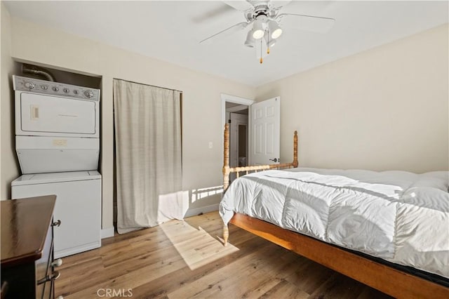 bedroom featuring ceiling fan, stacked washer / dryer, and hardwood / wood-style floors