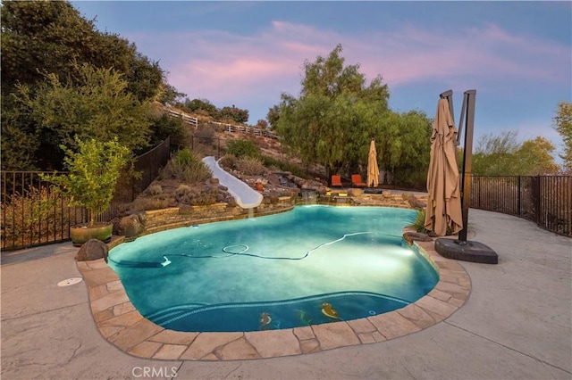 pool at dusk with a water slide and a patio