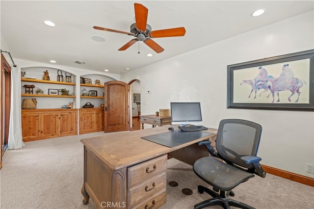 carpeted office space with ceiling fan and built in shelves