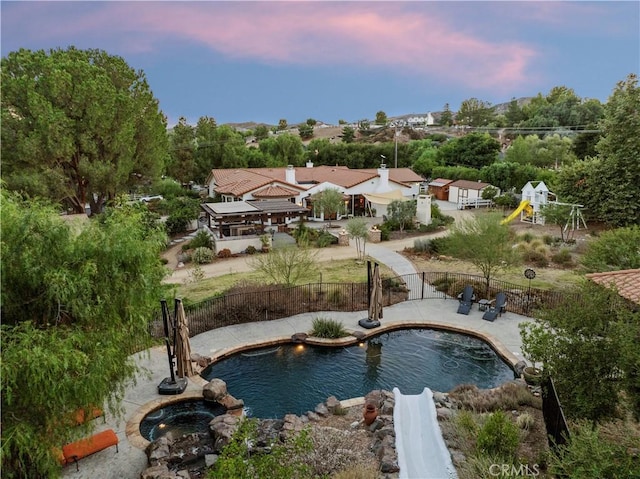 pool at dusk with a playground and an in ground hot tub