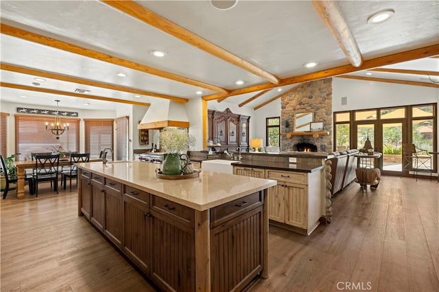 kitchen featuring decorative light fixtures, lofted ceiling with beams, a large island with sink, and a fireplace