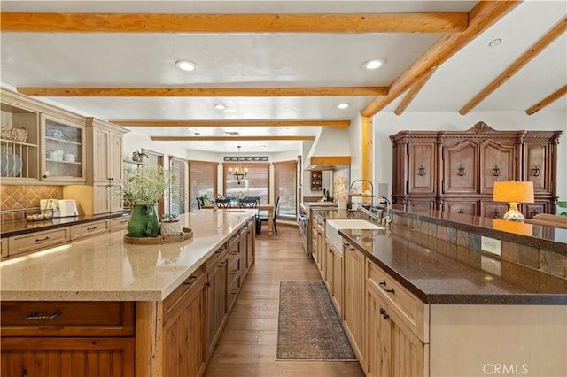 kitchen with dark stone counters, sink, backsplash, a large island, and light hardwood / wood-style flooring