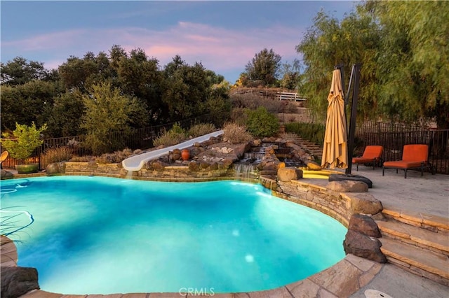 pool at dusk featuring a water slide and a patio