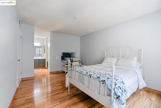 bedroom featuring ensuite bath, a textured ceiling, and hardwood / wood-style flooring