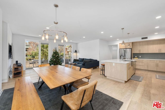 dining room with sink, an inviting chandelier, and light hardwood / wood-style flooring