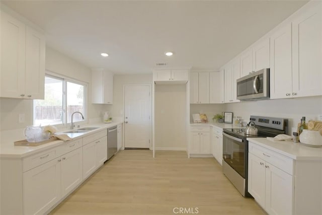 kitchen with light wood-type flooring, appliances with stainless steel finishes, white cabinets, and sink