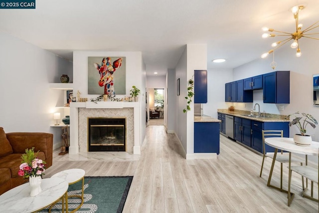 living room featuring a fireplace, sink, an inviting chandelier, and light hardwood / wood-style floors