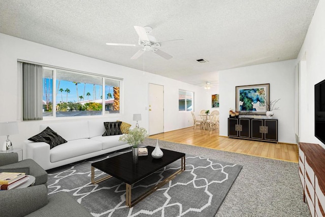 living room with a textured ceiling, ceiling fan, and hardwood / wood-style flooring