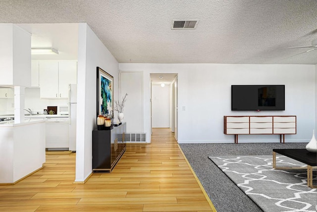 living room with a textured ceiling, ceiling fan, and light hardwood / wood-style flooring