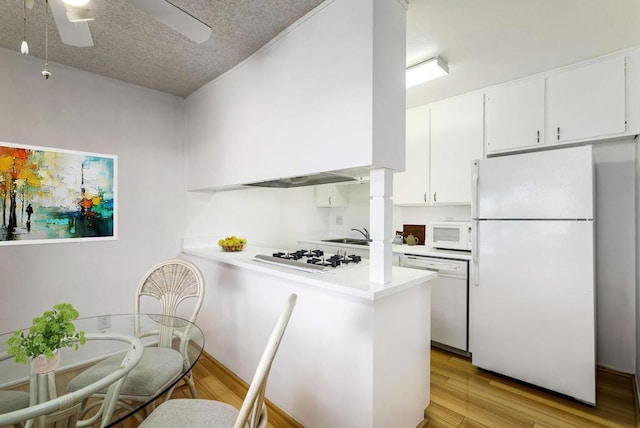 kitchen with kitchen peninsula, white appliances, white cabinets, a textured ceiling, and light hardwood / wood-style flooring