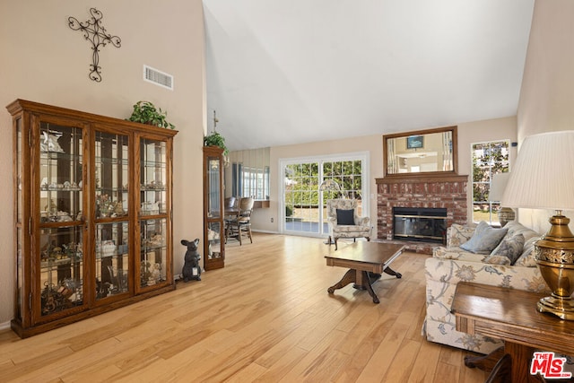 living room with a brick fireplace, light hardwood / wood-style floors, and high vaulted ceiling