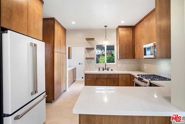 kitchen with kitchen peninsula, high end fridge, stainless steel gas stove, pendant lighting, and sink