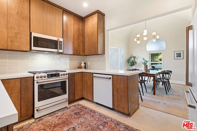 kitchen with appliances with stainless steel finishes, decorative light fixtures, backsplash, kitchen peninsula, and a notable chandelier