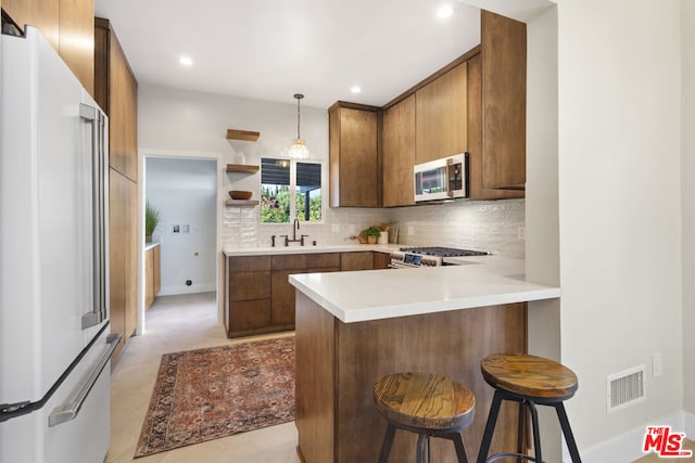 kitchen featuring kitchen peninsula, appliances with stainless steel finishes, a kitchen breakfast bar, hanging light fixtures, and sink