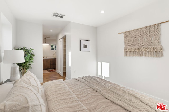 bedroom with a closet, connected bathroom, wood-type flooring, and sink