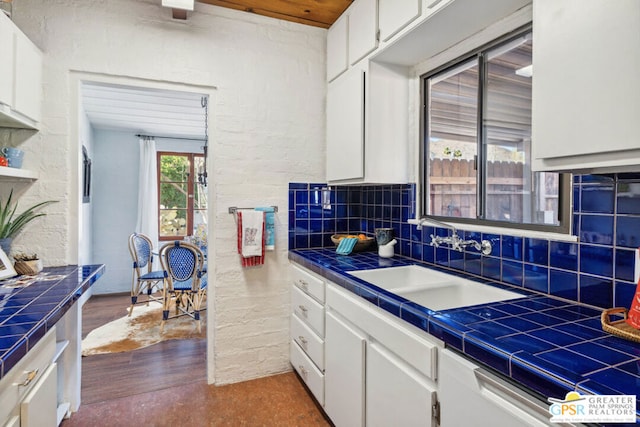 kitchen featuring tile countertops, decorative backsplash, white cabinets, and sink