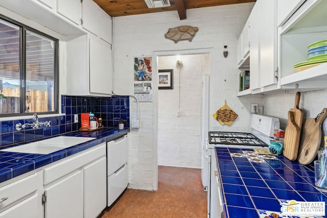 kitchen featuring white cabinetry, tile counters, beamed ceiling, brick wall, and sink