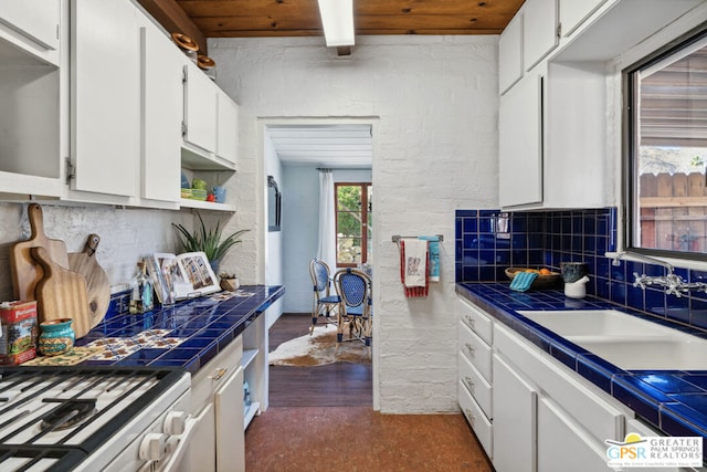 kitchen with tile counters, wood ceiling, white cabinets, and sink