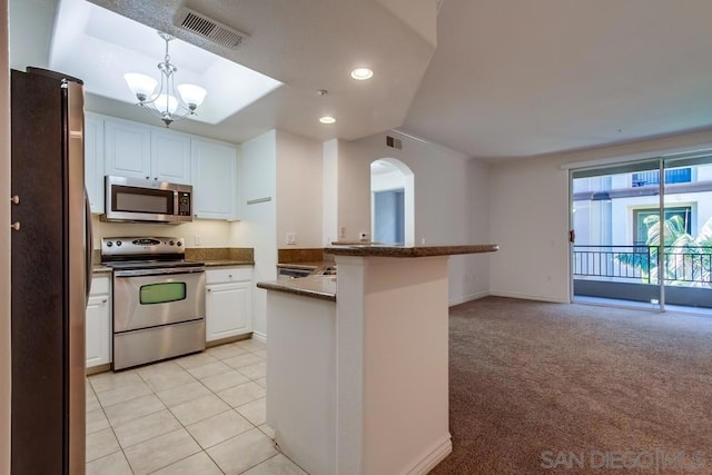 kitchen featuring appliances with stainless steel finishes, white cabinets, light colored carpet, a notable chandelier, and kitchen peninsula