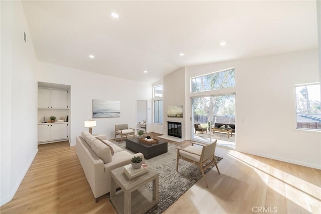 living room featuring a fireplace, a wealth of natural light, vaulted ceiling, and light wood-type flooring