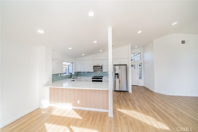 kitchen with white cabinets, appliances with stainless steel finishes, tasteful backsplash, kitchen peninsula, and vaulted ceiling