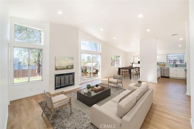 living room with high vaulted ceiling, light wood-type flooring, a large fireplace, and sink