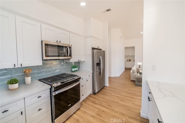 kitchen with appliances with stainless steel finishes, white cabinetry, decorative backsplash, light stone counters, and light hardwood / wood-style flooring