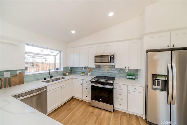 kitchen with white cabinetry, stainless steel appliances, sink, vaulted ceiling, and light stone counters