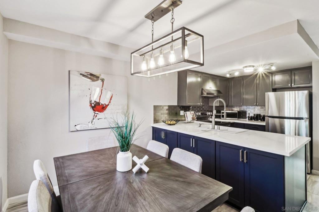 kitchen featuring hanging light fixtures, decorative backsplash, stainless steel refrigerator, and kitchen peninsula