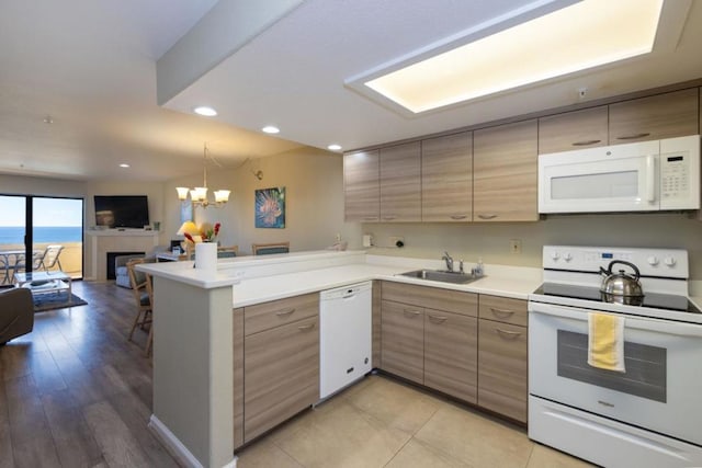 kitchen featuring kitchen peninsula, a tiled fireplace, white appliances, a chandelier, and sink