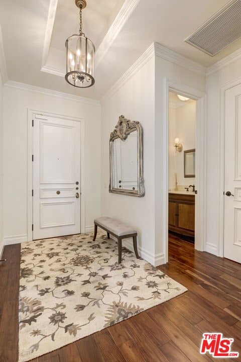 doorway featuring an inviting chandelier, ornamental molding, hardwood / wood-style flooring, and a tray ceiling