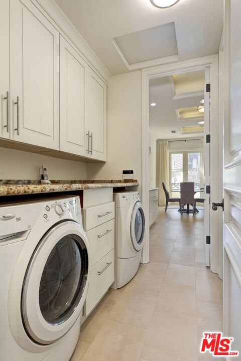 clothes washing area featuring cabinets, washer and clothes dryer, and light tile patterned flooring