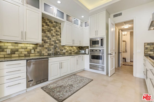 kitchen featuring white cabinets, appliances with stainless steel finishes, dark stone countertops, decorative backsplash, and sink