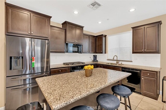 kitchen featuring stainless steel appliances, light stone countertops, a kitchen island, a breakfast bar, and sink