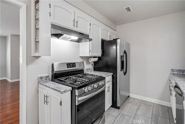 kitchen with appliances with stainless steel finishes, light stone counters, and white cabinetry