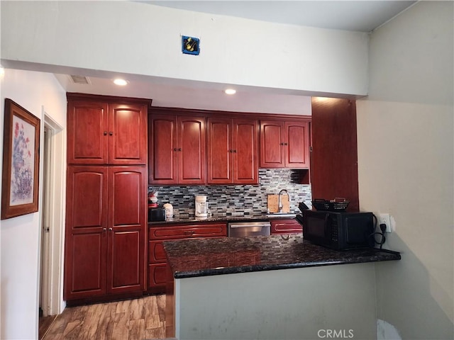 kitchen featuring sink, light hardwood / wood-style flooring, dark stone countertops, stainless steel dishwasher, and backsplash