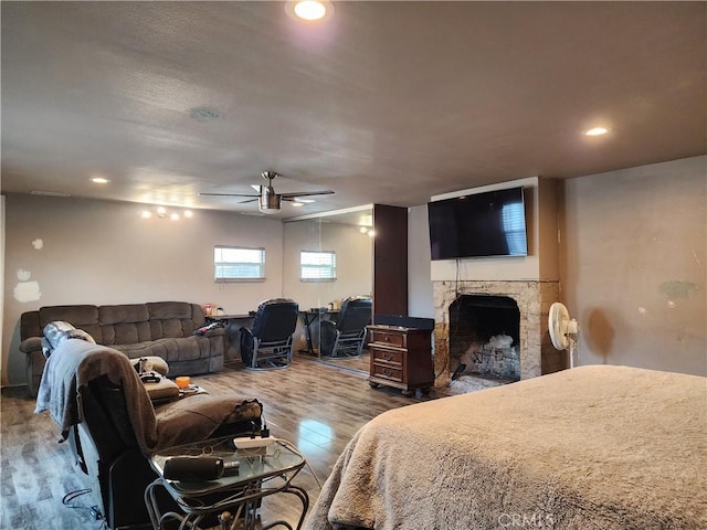 bedroom with ceiling fan, wood-type flooring, and a fireplace