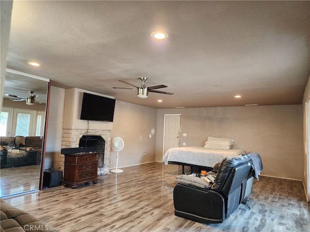 bedroom with ceiling fan, wood-type flooring, a stone fireplace, and a textured ceiling