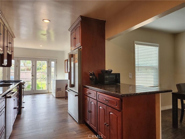 kitchen with french doors, dark stone countertops, appliances with stainless steel finishes, kitchen peninsula, and hardwood / wood-style flooring