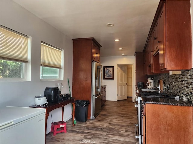 kitchen with stainless steel appliances, dark hardwood / wood-style floors, dark stone countertops, and decorative backsplash