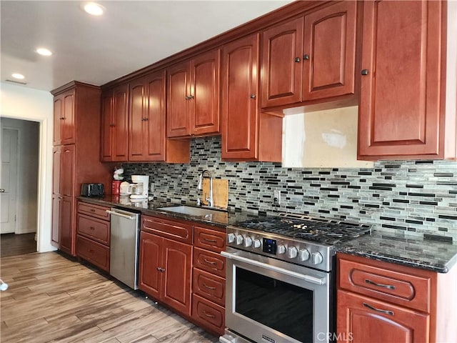 kitchen featuring appliances with stainless steel finishes, tasteful backsplash, sink, dark stone counters, and light hardwood / wood-style floors