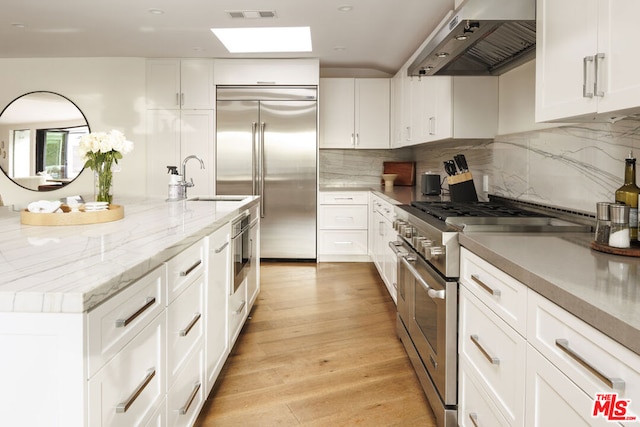 kitchen featuring sink, white cabinets, exhaust hood, and high quality appliances