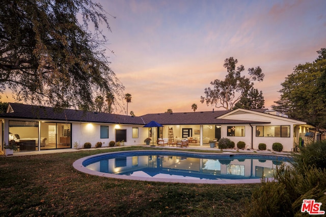 pool at dusk featuring a yard and a patio