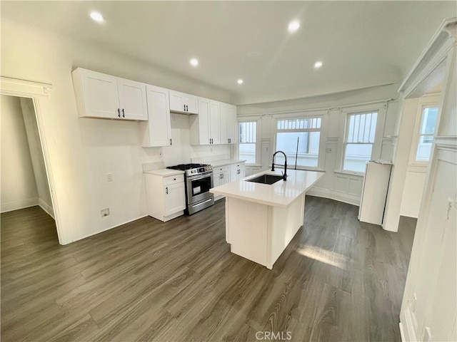 kitchen featuring white cabinetry, a center island with sink, stainless steel gas range, dark wood-type flooring, and sink