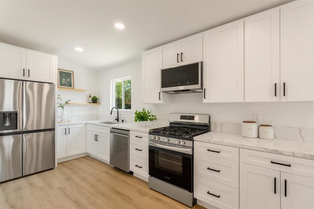 kitchen featuring appliances with stainless steel finishes, white cabinetry, light hardwood / wood-style floors, sink, and light stone counters