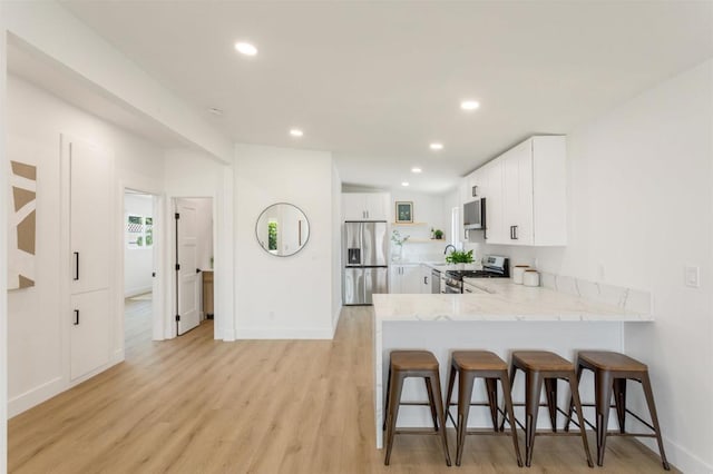 kitchen with white cabinetry, kitchen peninsula, stainless steel appliances, and a breakfast bar area